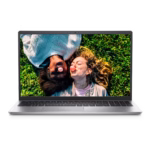 Vista frontal del portátil Dell Inspiron 3520 plateado abierto. La pantalla muestra una imagen de dos personas acostadas en el césped haciendo burbujas de chicle. El teclado es visible debajo de la pantalla.