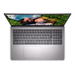 Vista cenital de un portátil Dell Inspiron 3520 plateado abierto, mostrando el teclado, el touchpad y la pantalla con una imagen de dos personas acostadas en el césped.